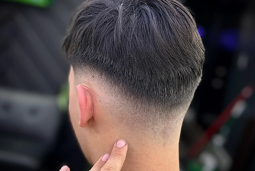 Degradado bajo en la nuca, limpio hasta el cuello, con el barbero señalando la línea con el dedo