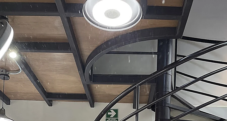 La escalera de caracol de herrería negra al centro del local, bajo el techo de vigas de madera y una lámpara redonda