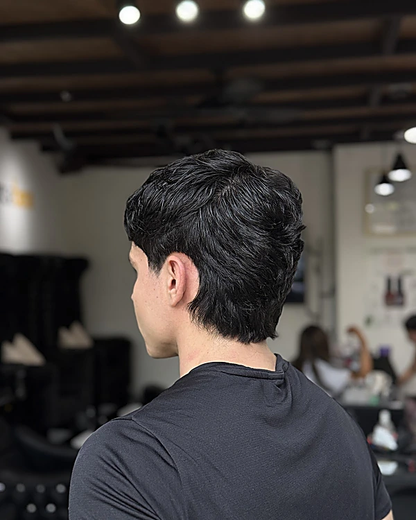 Interior del local con techo de vigas de madera y focos colgantes, un cliente de espaldas con el corte terminado