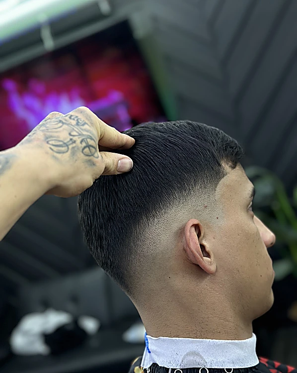 Mano tatuada del barbero acomodando el cabello de un corte con degradado bajo